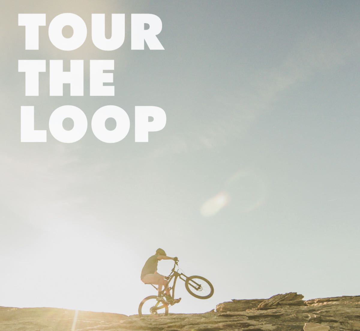 TOUR THE LOOP (cyclist doing a wheelie on the top of the cliffs)
